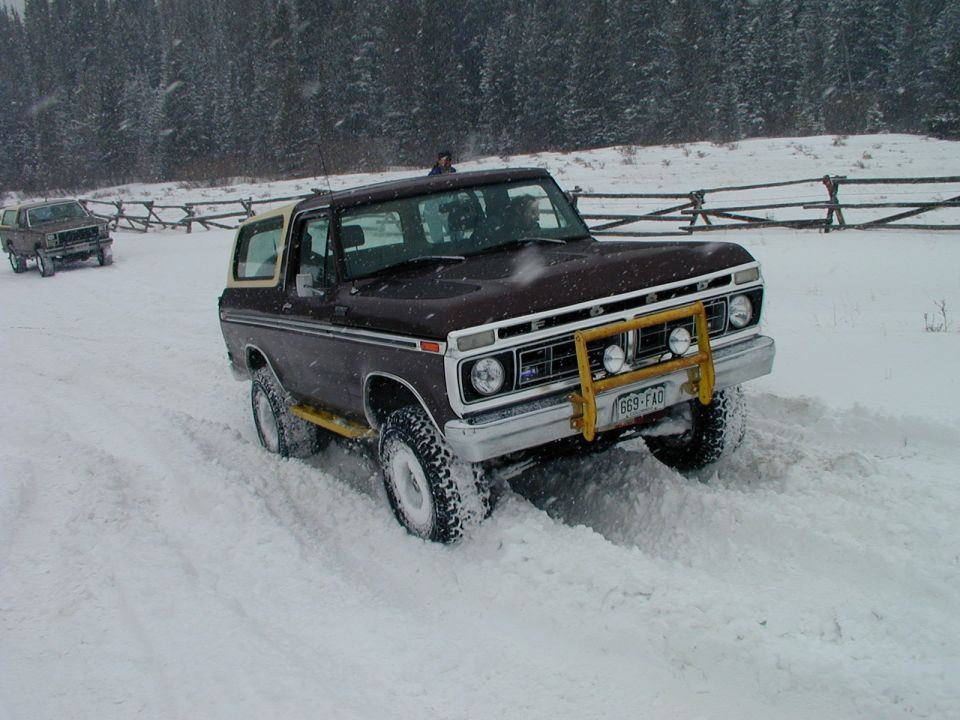 Brown 1979 Ford Bronco with yellow bull bar driving in snow, another vehicle behind