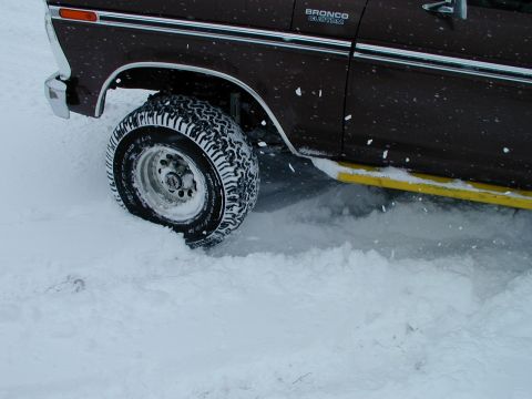 1979 Ford Bronco - A dark brown Ford Bronco is partially submerged in snow and ice, with its front wheel stuck.