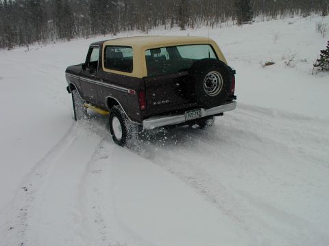 1979 Ford Bronco - A Ford Bronco navigates a snowy path, kicking up snow as it drives.