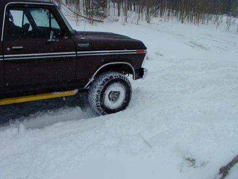 1979 Ford Bronco - A 1979 Ford Bronco navigates through a snowy landscape, kicking up snow as it drives.