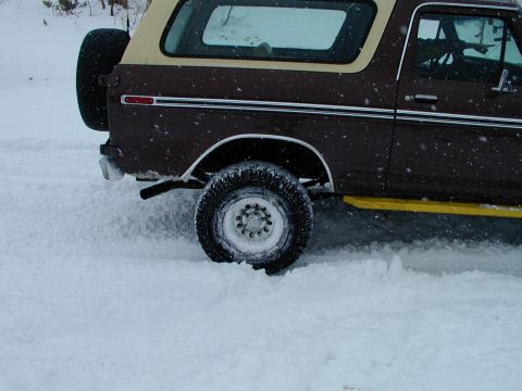1979 Ford Bronco - Brown 1978 Ford Bronco with tan top driving through snow, spare tire visible on rear.
