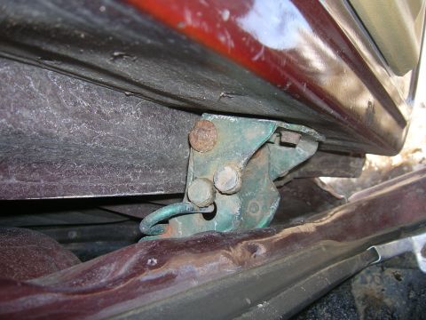 1979 Ford Bronco - Close-up of a vehicle's door hinge mechanism, showing green paint and signs of rust.