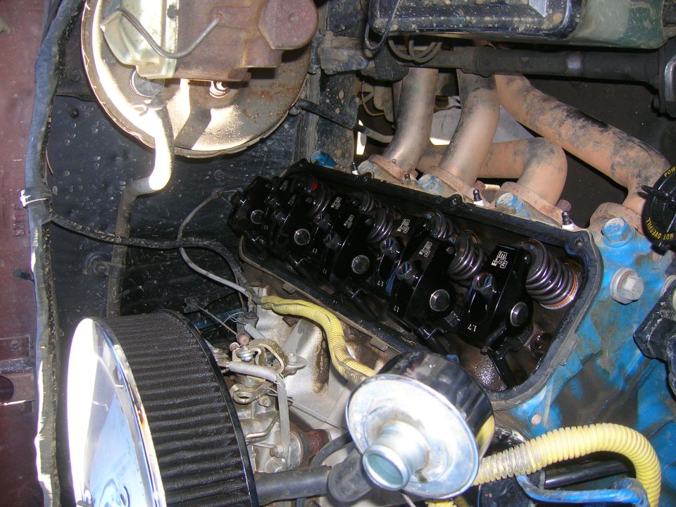 Close-up of an engine with the valve cover off, showing the rocker arms and springs. Air filter and brake booster visible