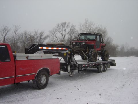 1992 Ford Bronco - A red off-road vehicle is transported on a trailer through a snowy landscape.