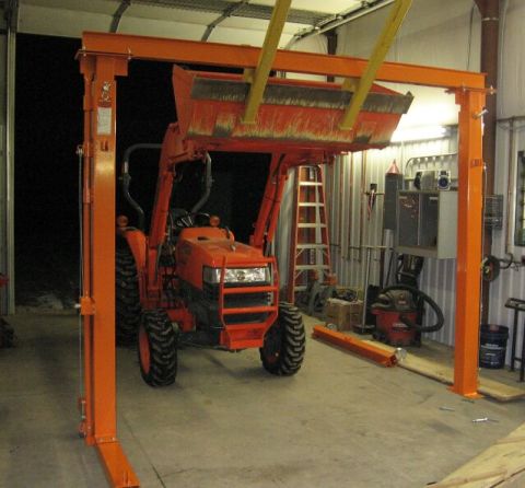 1990 Ford Bronco - An orange tractor with a front loader is positioned under a gantry lift in a workshop.