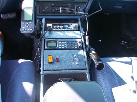 1999 Ford Crown Victoria - The interior of a police vehicle shows a console equipped with communication devices and a gear shift.