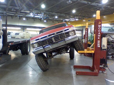 1974 Ford F-250 - A red Ford truck is elevated on a lift in a garage, showing its front grille and tires.