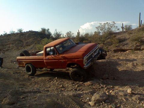 1974 Ford F-250 - This orange 1974 Ford F-250 navigates a challenging rocky terrain, with another vehicle visible in the background.