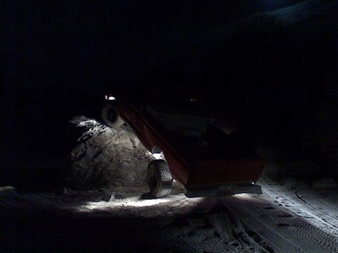 1974 Ford F-250 - A red pickup truck is seen on its side in a dark, possibly snowy, environment, illuminated by its own headlights.