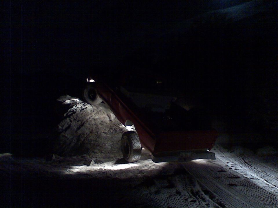 Red pickup truck on its side at night, with headlights illuminating the scene