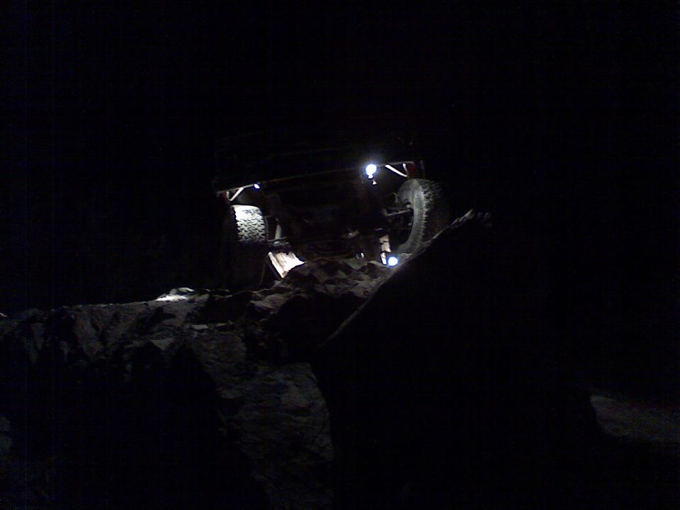 Off-road vehicle with lights on, navigating rocky terrain in the dark