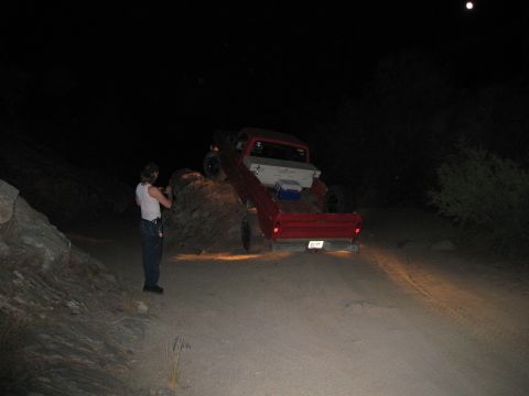 1974 Ford F-250 - A person photographs a red pickup truck navigating a rocky dirt path under the moonlight.