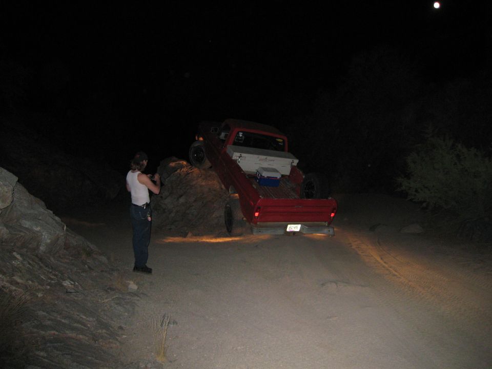 Red pickup truck with a white toolbox in the bed, angled on a dirt incline at night
