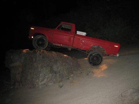 1974 Ford F-250 - This red pickup truck is shown off-roading, climbing over a large rock in a nighttime scene.
