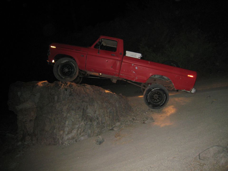 Red pickup truck with lifted suspension navigating a large rock off-road