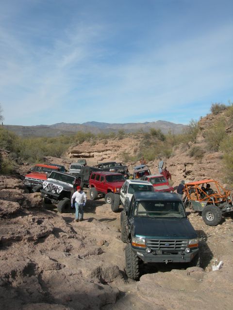 1974 Ford F-250 - A group of off-road vehicles travels through a rocky desert landscape under a partly cloudy sky.