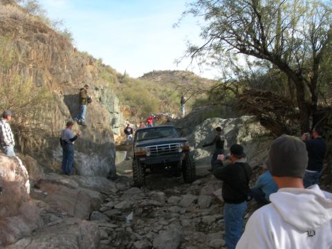 1974 Ford F-250 - A dark blue pickup truck tackles a challenging rocky terrain during an off-road event.