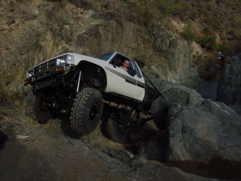 1986 Toyota Hilux - A heavily modified white pickup truck navigates a challenging rocky trail.