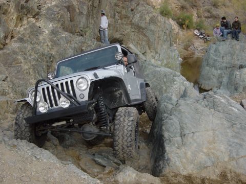 1986 Toyota Hilux - Off-road Jeep Wrangler TJ tackles a challenging rocky trail with spectators watching.