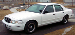 1999 Ford Crown Victoria - This white sedan is parked outside on a paved surface with a sidewalk and some grass visible in the background.