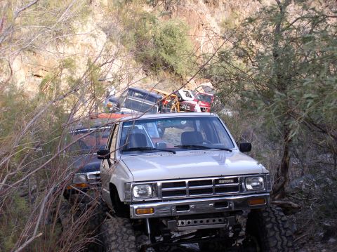 1986 Toyota Hilux - Several off-road trucks are parked closely together in a brushy, dry creek bed.