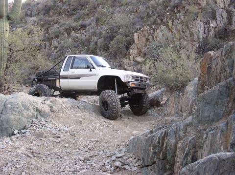 1986 Toyota Hilux - This heavily modified pickup truck navigates a challenging rocky trail in a desert environment.