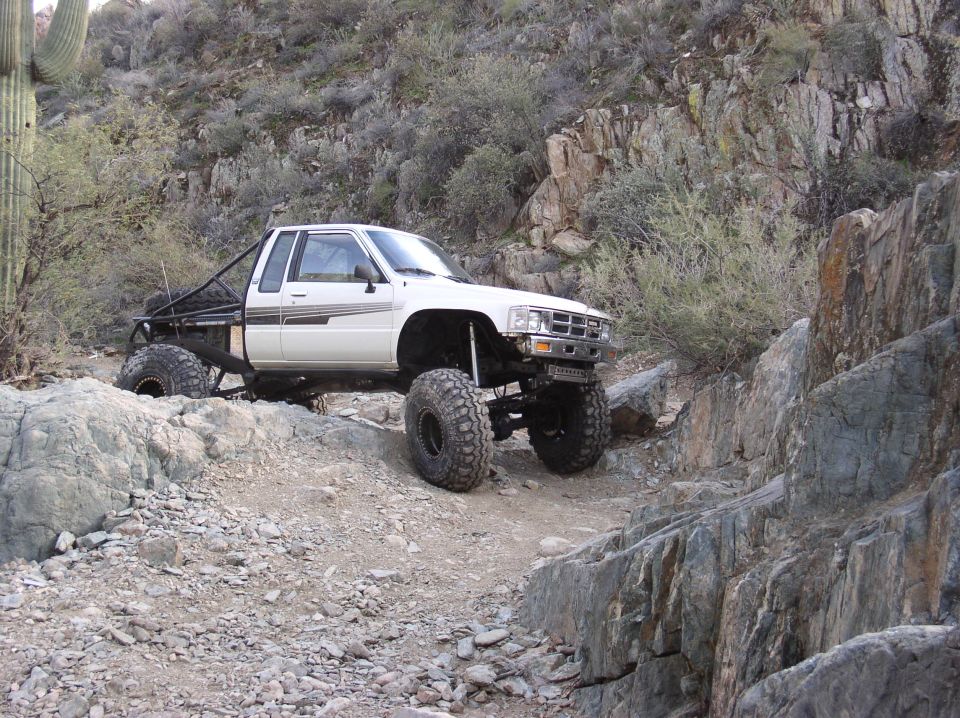 White pickup truck with huge tires and roll cage driving on rocky terrain