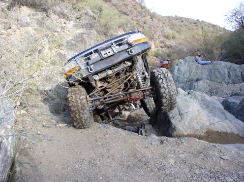 1986 Toyota Hilux - An off-road truck navigates a rocky terrain, with another vehicle and a person observing the challenging path.