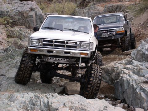 1986 Toyota Hilux - Two modified trucks navigate a challenging rocky trail, their off-road capabilities.