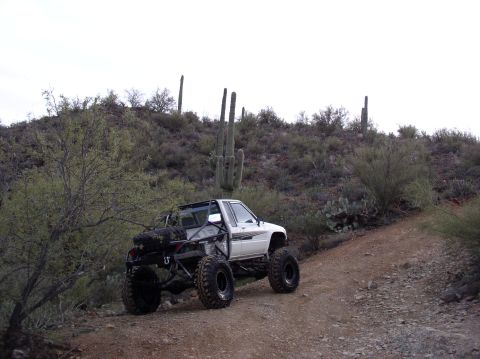 1986 Toyota Hilux - A modified pickup truck navigates a dusty trail through a desert environment with saguaro cacti.