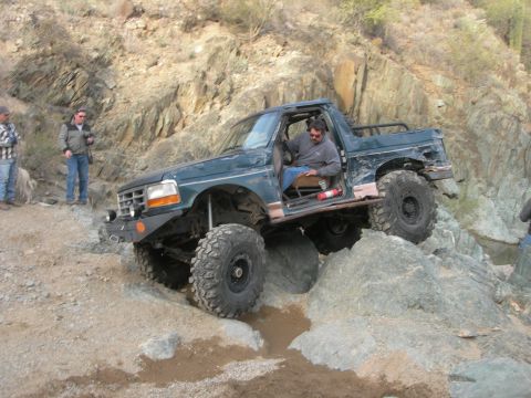 1974 Ford F-250 - A modified Ford Bronco navigates a rocky off-road trail with a driver at the wheel.