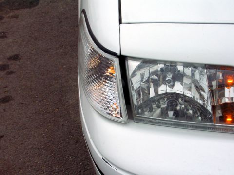 1999 Ford Crown Victoria - Close-up of the front corner of a white 1999 Ford Crown Victoria, showing the clear turn signal and headlight assembly.