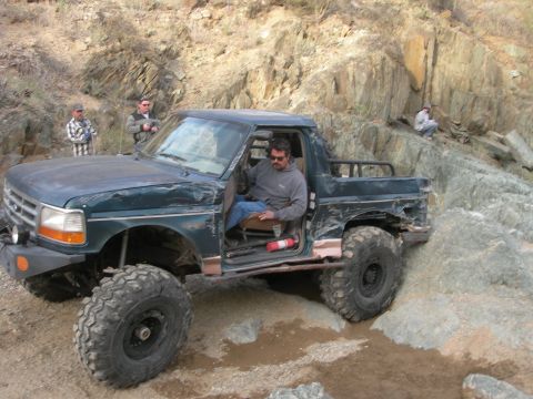 1974 Ford F-250 - A modified Ford pickup navigates rocky terrain with a driver inside.
