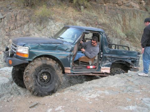 1974 Ford F-250 - A modified Ford Bronco navigates a challenging rocky trail with a passenger observing.