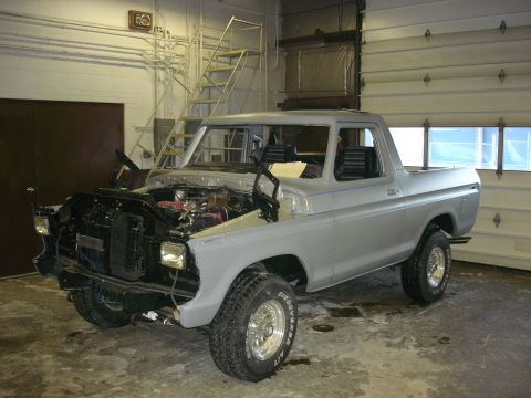 1979 Ford Bronco - A gray Ford Bronco is undergoing work in a garage, with its hood open to reveal the engine compartment.