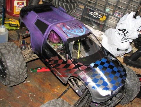 1999 Ford F-150 - A custom-painted RC monster truck with a visible engine sits on a cluttered workbench.