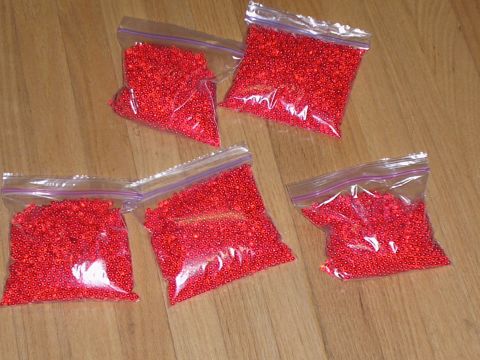 1990 Ford Bronco - Five bags of red beads are spread out on a wooden surface.