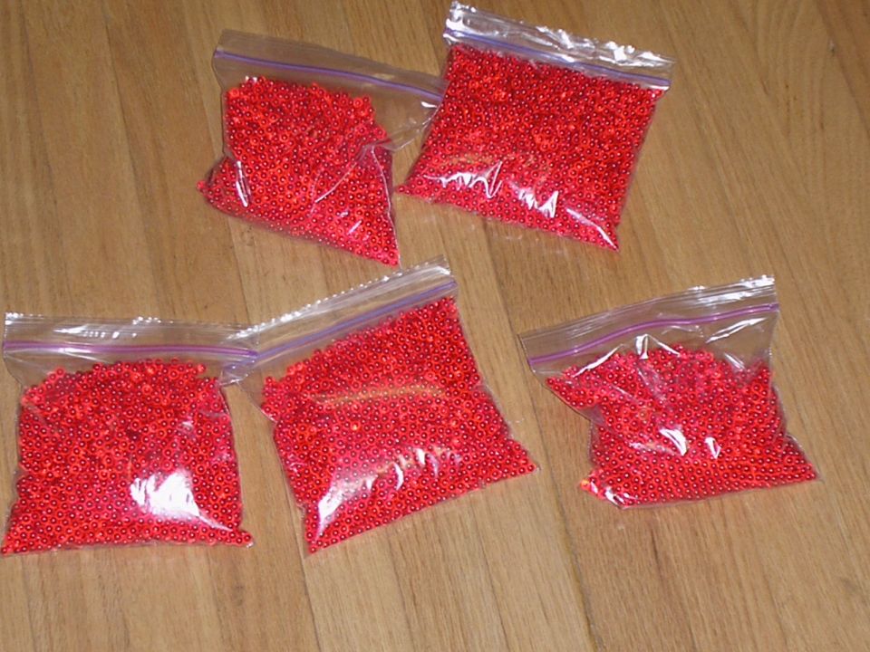 Five plastic bags filled with small red beads on a wooden floor