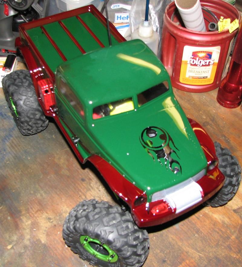 Green and red RC rock crawler truck with large tires on a wooden surface