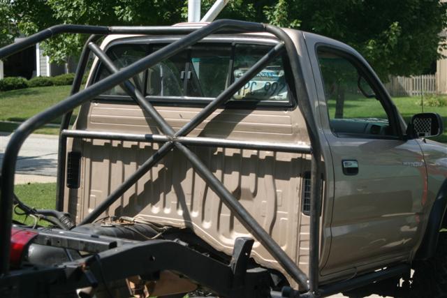 Tan regular-cab pickup with external X-braced roll cage and exposed rear frame, parked on a street