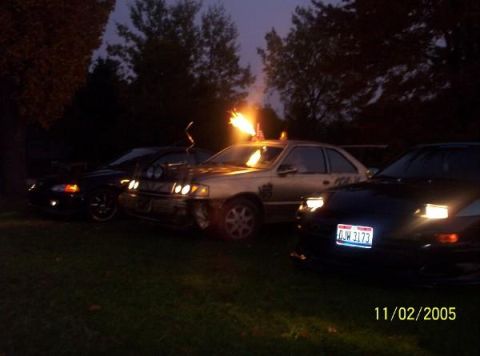 1993 Mercury Topaz - Cars parked outdoors at night with flames coming from the roof of the middle vehicle.