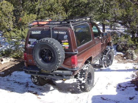 1986 Ford Bronco II - This 1986 Ford Bronco II is equipped for off-road adventures, with large tires and a roof rack, seen in a snowy, wooded landscape.