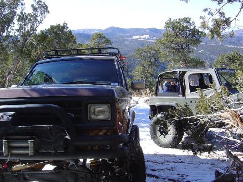 1986 Ford Bronco II - Two SUVs, including a 1986 Ford Bronco II, are parked on a snowy trail with mountains in the background.