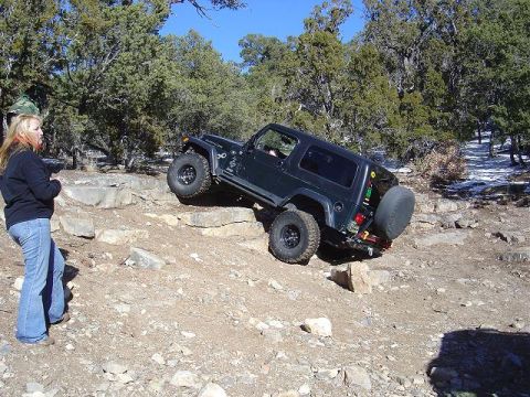 1986 Ford Bronco II - A black Jeep Wrangler Rubicon navigates a rocky off-road trail with a woman observing.