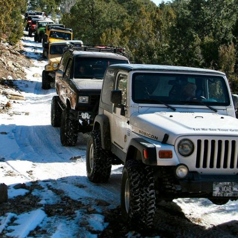 1986 Ford Bronco II - A convoy of modified off-road vehicles navigates a snow-covered trail through a wooded area.