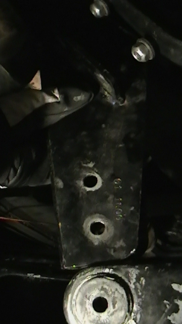 1995 Ford Bronco - Close-up of a black metal axle pivot bracket, showing two bolt holes and stamped markings.