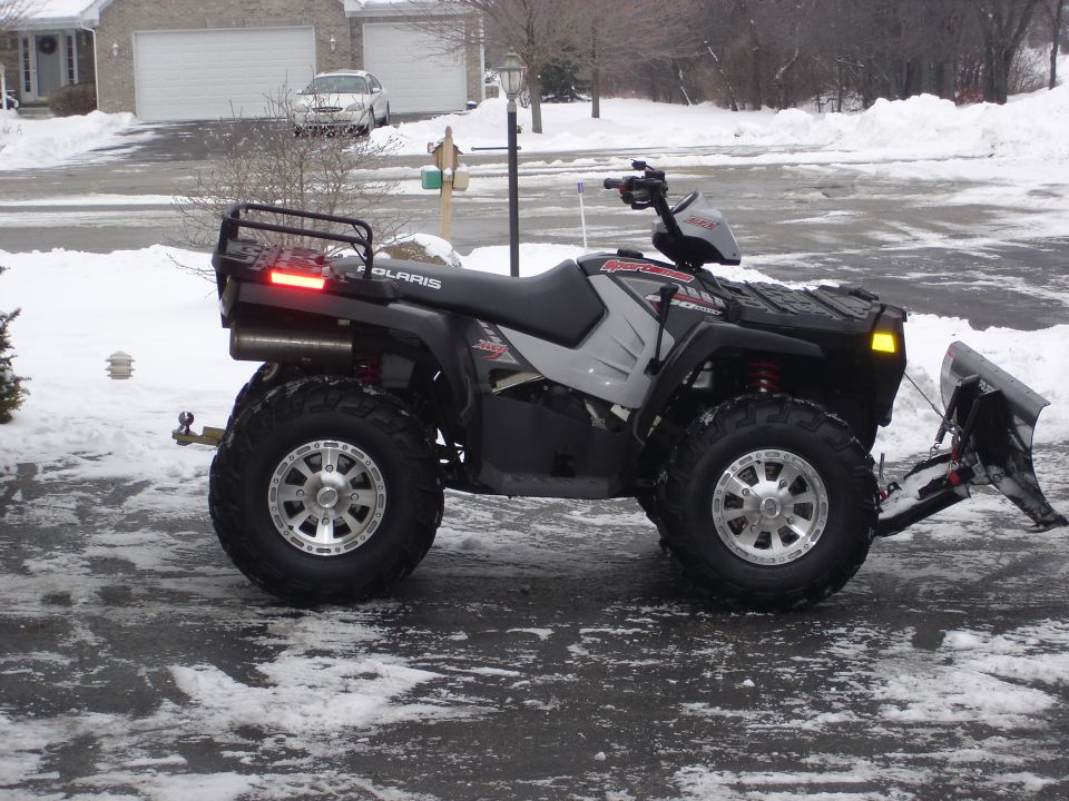Black Polaris ATV with a front plow attachment and snow on the ground