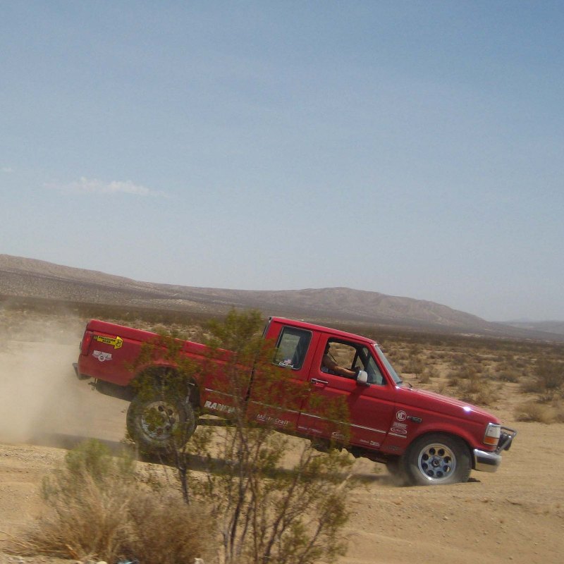 Red 1996 Ford F-150 pickup truck driving off-road