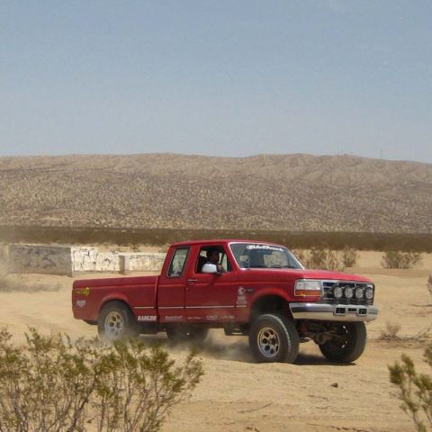 1996 Ford Bronco - Red 1995 Ford F-250 extended cab pickup truck driving off-road in a desert.