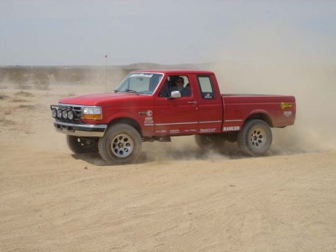 1996 Ford Bronco - A red pickup truck navigates a dusty off-road environment.